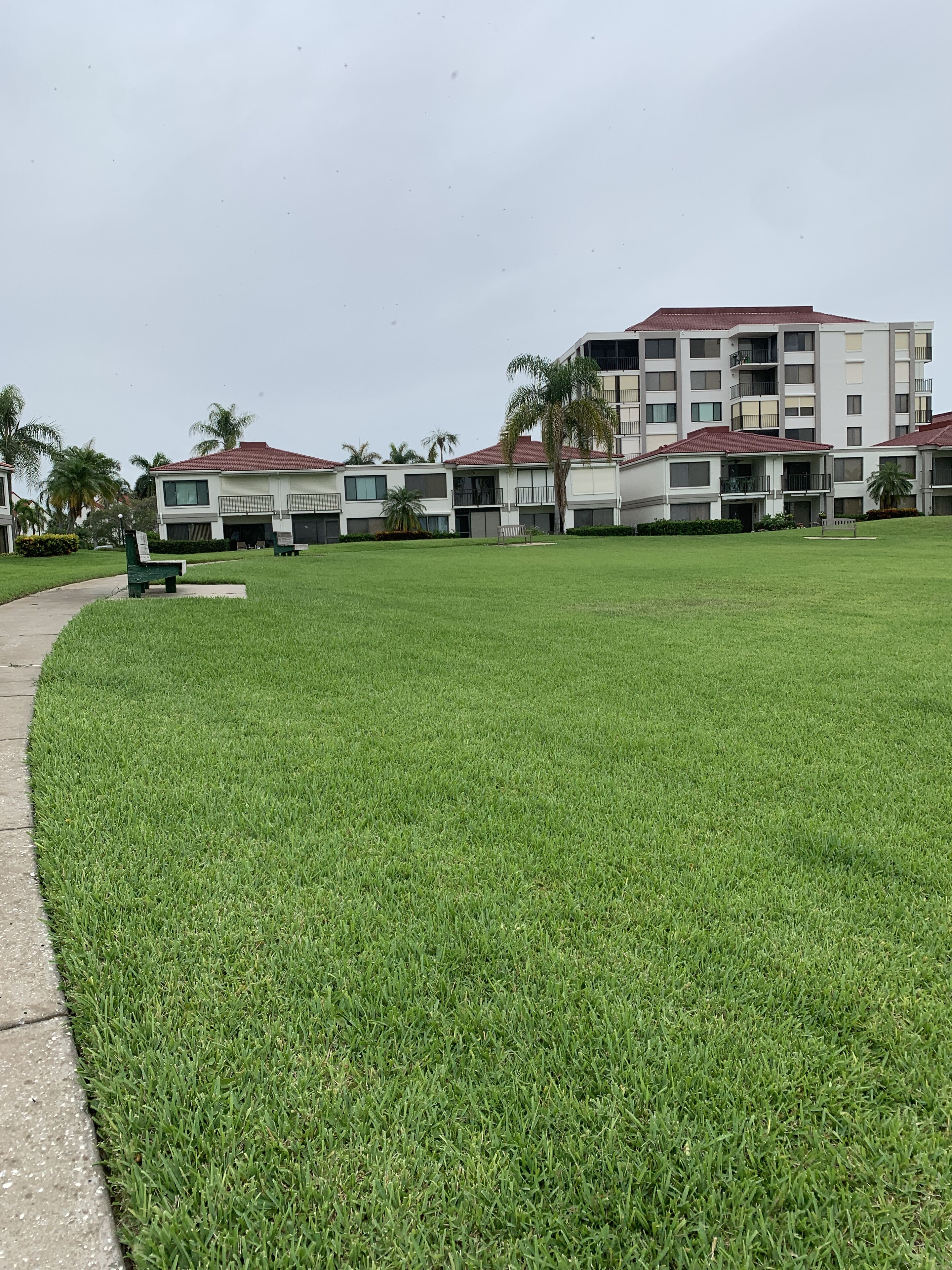 A grassy area with a pathway leading to a building with multiple balconies and a red roof.