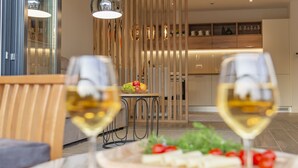 A modern dining area with two wine glasses on a table, a fruit bowl, and a wooden partition in the background. - Lustica Bay Central (Radovici)