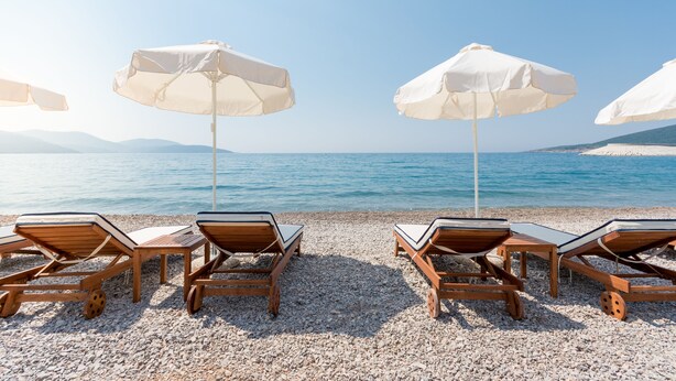 A beach with wooden lounge chairs and white umbrellas. - Lustica Bay Central (Radovici)