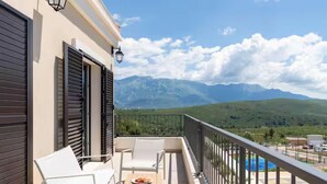 A balcony with white chairs and a table, overlooking a mountainous landscape. - Lustica Bay Central (Radovici)
