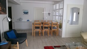 Ett modernt vardagsrum med en matplats, med en svart fåtölj, ett soffbord i glas och ett matbord i trä med stolar.