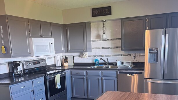 A modern kitchen with grey cabinets, a stainless steel refrigerator, a microwave, and a coffee maker.