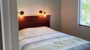 A bedroom with a bed, a ceiling fan, two wall-mounted lights, and a window with blinds.