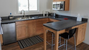 A modern kitchen with wooden cabinets, a stainless steel refrigerator, a microwave, and a sink.