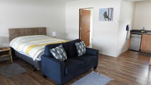 A bedroom with a bed, a sofa, a desk, and a door leading to a bathroom.
