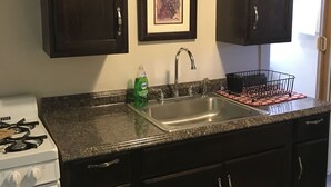 Cocina con gabinetes de madera oscura, un lavamanos de acero inoxidable, un escurreplatos y una obra de arte enmarcada sobre el lavamanos.