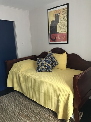Een slaapkamer met een bed, een kussen, een ingelijste foto aan de muur en een deur.
