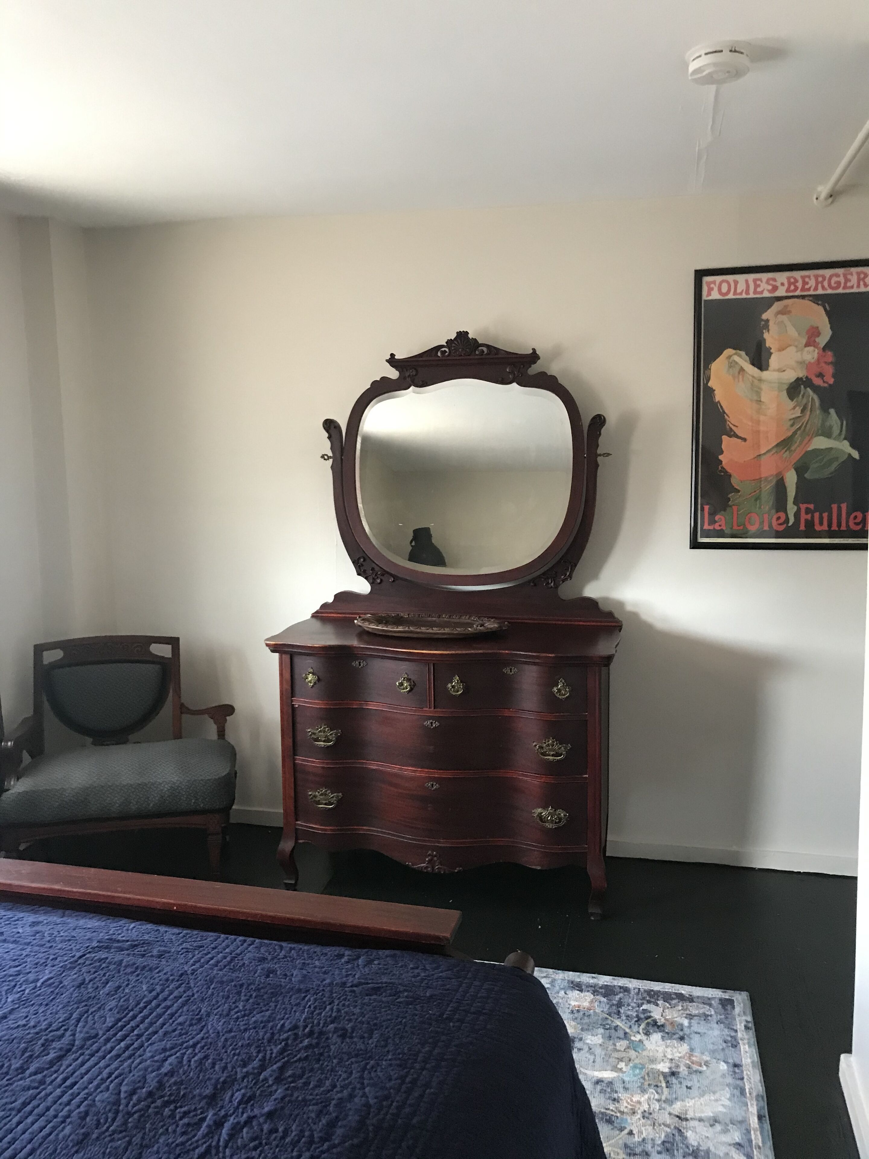 A bedroom with a large bed, a dresser with a mirror, a chair, and a poster on the wall.
