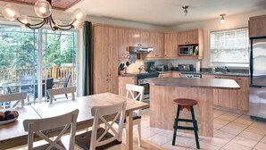 Une cuisine moderne avec des meubles en bois, un îlot central et un coin repas offrant une vue sur l’extérieur.
