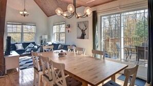 Un vaste espace de vie comprenant une grande table à manger en bois, un coin salon confortable et une vue sur l’extérieur grâce à de grandes fenêtres.