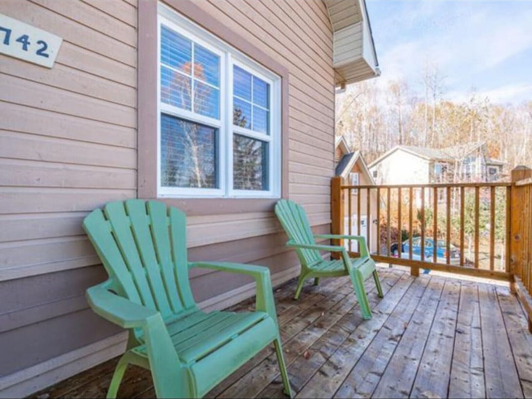 Una terraza de madera con dos sillas Adirondack verdes y una valla de madera.