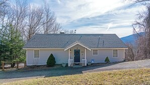 A single-story house with a dark front door, a small porch with two chairs, and a small tree in front. - Birds Nest- Hot Tub w/ Mtn View, Whirlpool Bath, Gas Grill, Keyless Entry (Seven Devils)