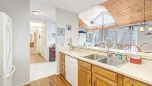A kitchen with wooden cabinets, a dishwasher, a sink, and a window with curtains. - Birds Nest- Hot Tub w/ Mtn View, Whirlpool Bath, Gas Grill, Keyless Entry (Seven Devils)
