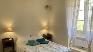 En pænt redt seng med blomstret sengetøj, to sengeborde med lamper og et vindue med gardiner.