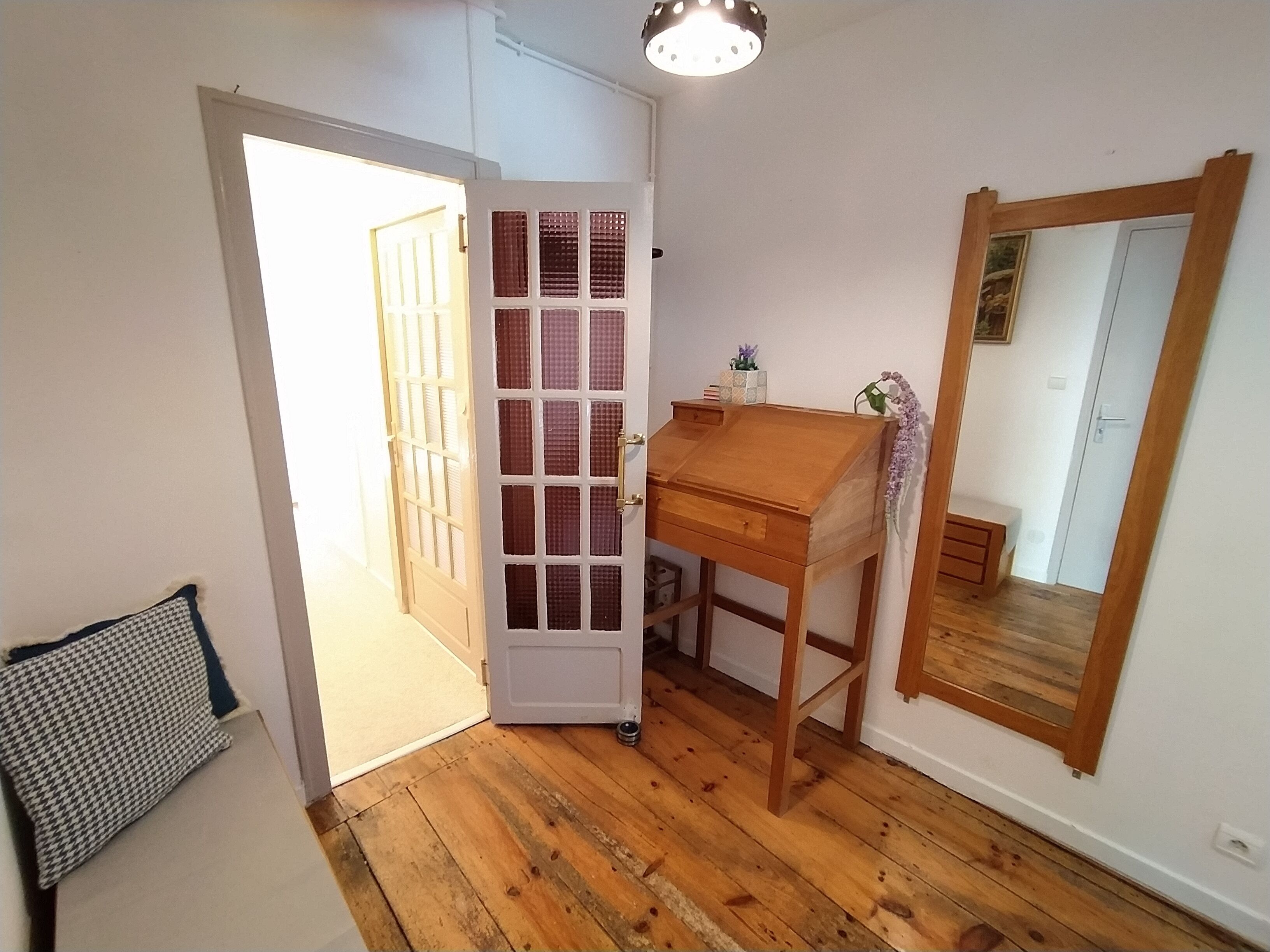 Une pièce avec un plancher en bois, un bureau avec des tiroirs, un miroir et une porte avec une fenêtre.