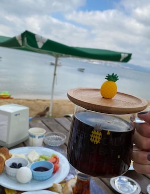 A beachside picnic with a mug, plate of food, and a view of the sea. - Mete Otel (Erdek)