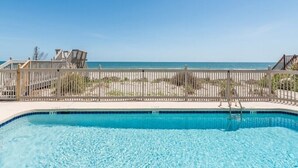 A clear blue swimming pool with a wooden deck and a view of the beach and ocean. - Sea-breezin' - Beachfront Condo                   (Surfside Beach)
