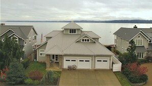 A residential area with houses, a driveway, and a body of water in the background. - Beach house no-bank waterfront 4-bedroom vacation home on Camano Island (Camano)