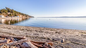 A calm lake with a sandy beach and scattered logs. - Beach house no-bank waterfront 4-bedroom vacation home on Camano Island (Camano)