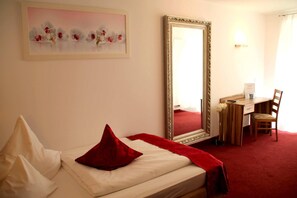 A hotel room with a bed, a desk, a chair, a large mirror, and a painting on the wall.