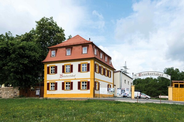 A two-story building with a yellow and white facade, a red roof, and a sign that reads "Bruckertshof."