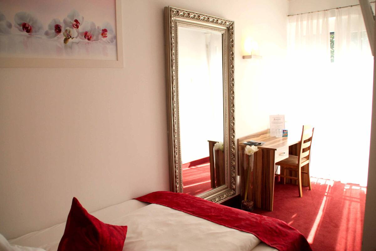 A hotel room with a bed, a large mirror, a desk, and a chair.