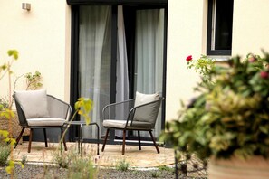 An outdoor seating area with two chairs and a table, a sliding glass door, and a potted plant.