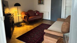En stue med sofa, sofabord, lampe, tæppe og en dør.