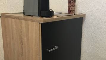 A small wooden cabinet with a black door, a coffee maker on top, and a can of coffee on the side.