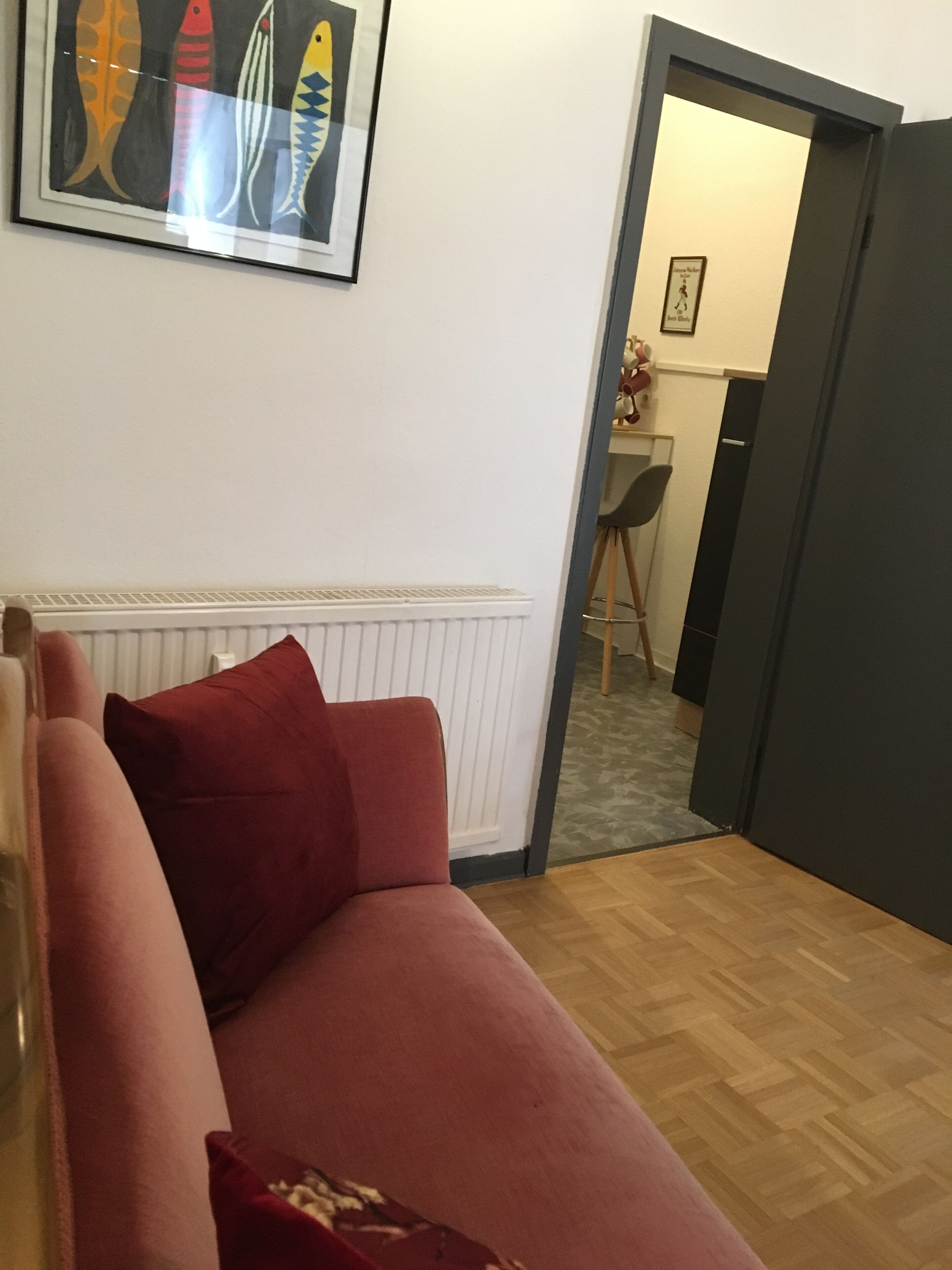 Uma sala de estar com um sofá vermelho, um radiador e uma pintura de peixes emoldurada na parede.