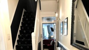 A staircase with black carpet and white balusters, leading to a room with a red sofa and a mirror on the wall. - The Sandalwood (Blackpool)