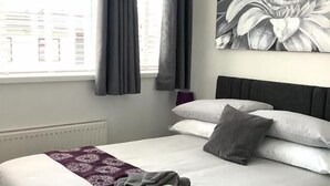 A neatly made bed with white and grey bedding, a grey throw blanket, and a floral-patterned pillow. - The Sandalwood (Blackpool)