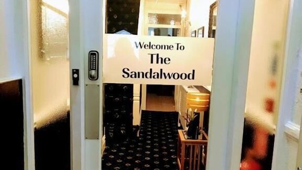 A hotel entrance with a welcome sign, a black patterned carpet, and a chandelier. - The Sandalwood (Blackpool)
