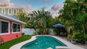 Una piscina de diseño curvo, rodeada por un césped cuidado y diversas plantas tropicales.