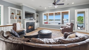A living room with a fireplace, leather sofa, and a view of the outdoors. - COZY, LUXURY LAKE HOUSE W/ STUNNING LAKE VIEWS!! (Lake Hamilton)