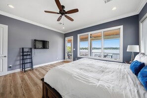 A bedroom with a large bed, a ceiling fan, a TV, and a balcony with a view.