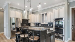 A modern kitchen with white cabinets, stainless steel appliances, and a central island with bar stools. - COZY, LUXURY LAKE HOUSE W/ STUNNING LAKE VIEWS!! (Lake Hamilton)