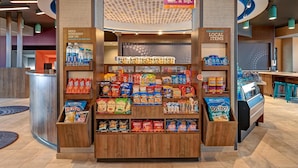 Un kiosque proposant une variété d’aliments emballés, une sélection de boissons et une affiche publicitaire pour un marché ouvert 24 heures sur 24, 7 jours sur 7.