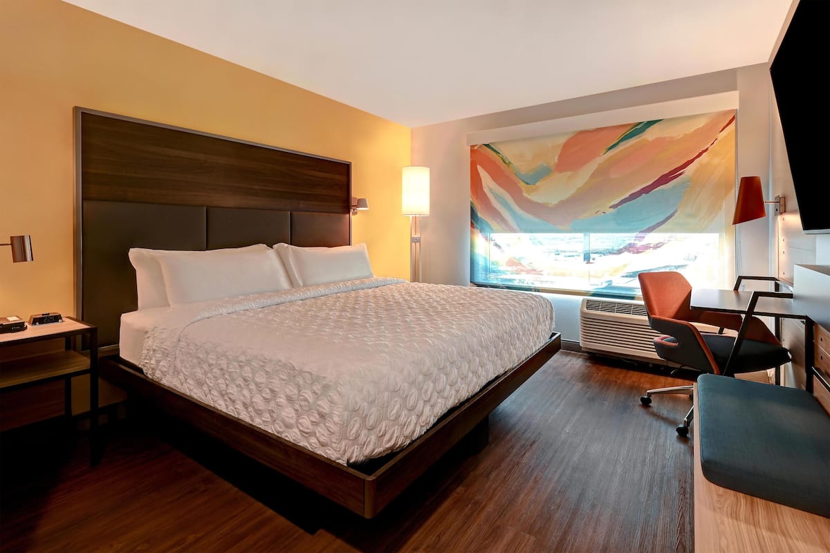 Une chambre d’hôtel moderne, dotée d’un grand lit, d’un bureau, d’une chaise et d’une grande fenêtre offrant une belle vue.