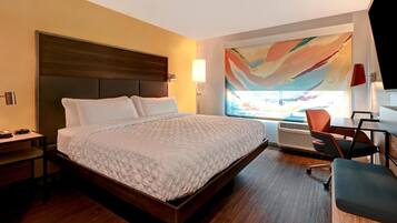 A modern hotel room with a large bed, a desk, a chair, and a large window with a view.