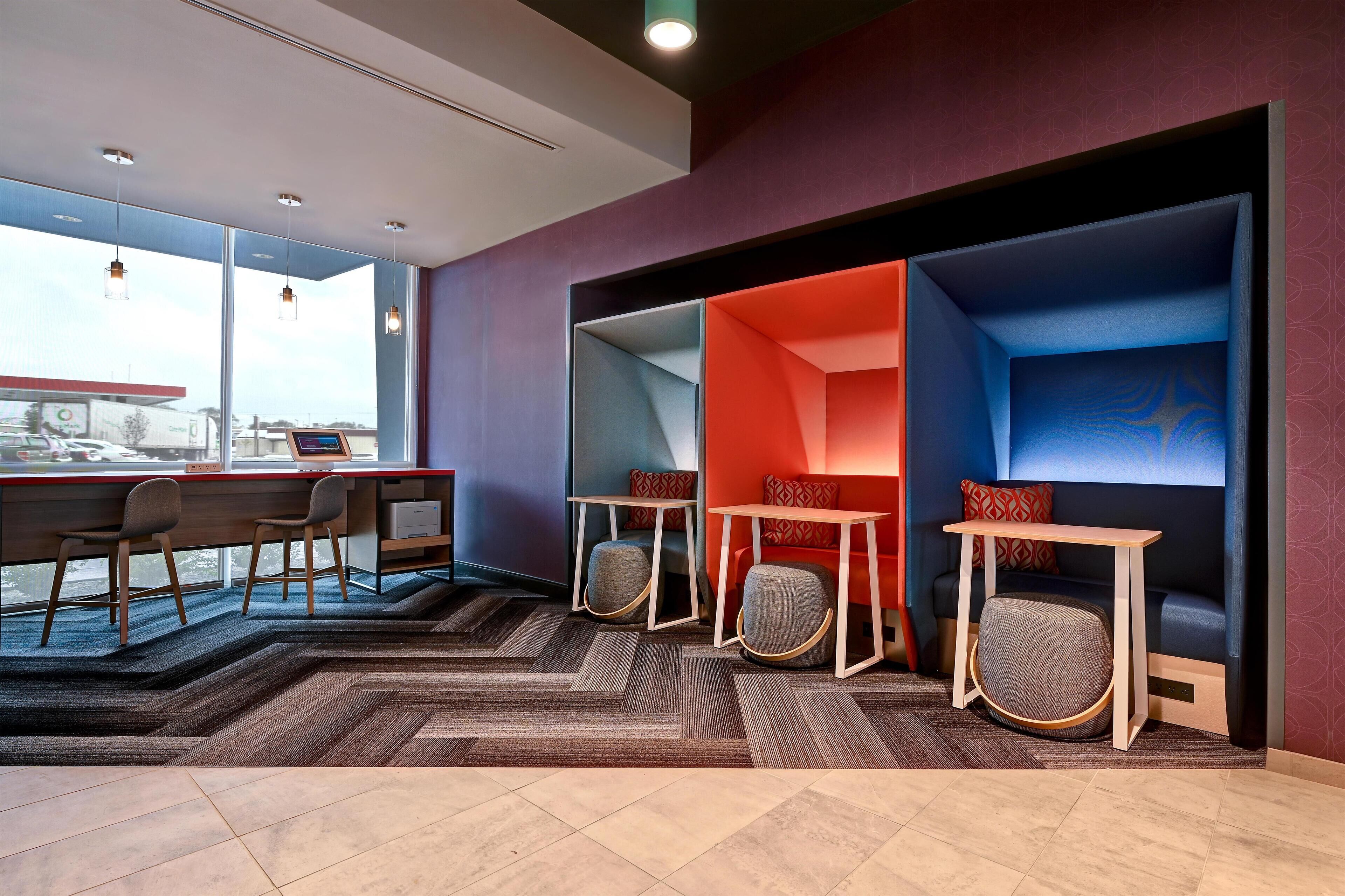 A modern office space with a large window, a desk with chairs, and a seating area with a sofa and tables.