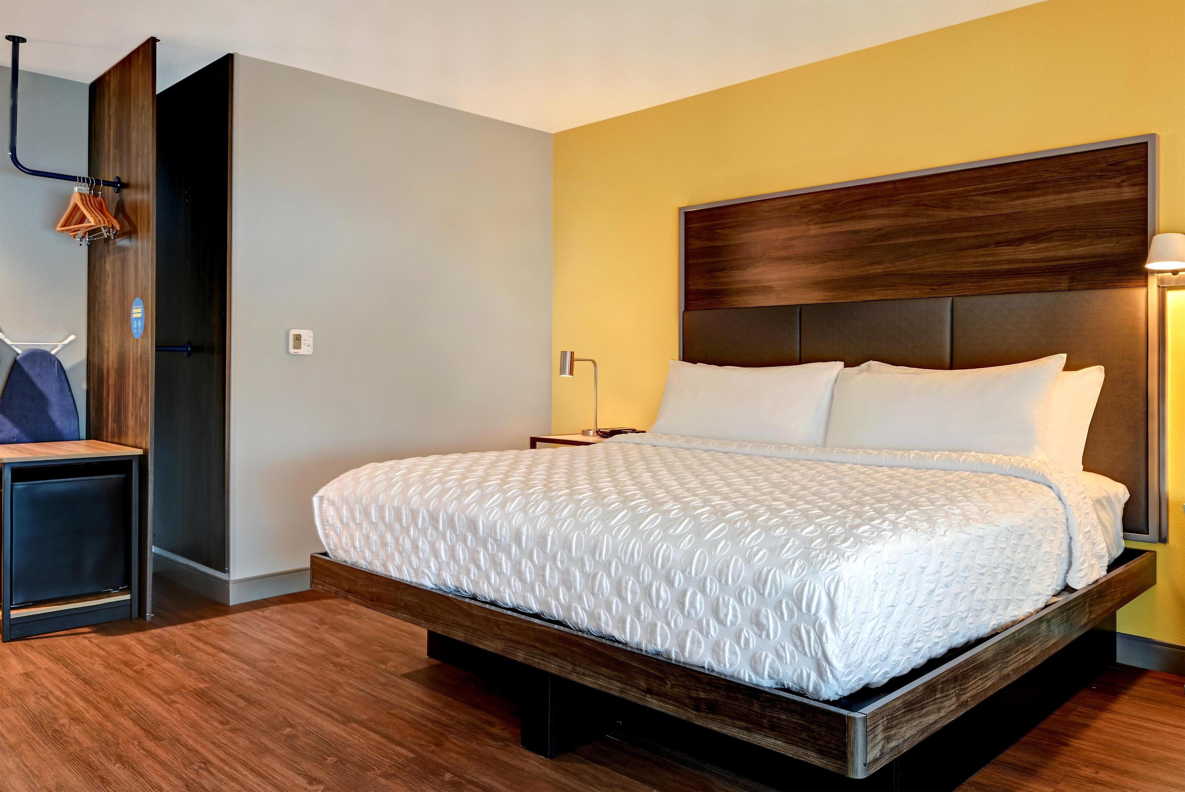 A modern hotel room with a large bed, wooden headboard, and a small bedside table.