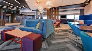 Un hall d’entrée moderne avec un canapé bleu, des sièges rouges et violets, une table basse en bois et un tapis à motifs chevrons.
