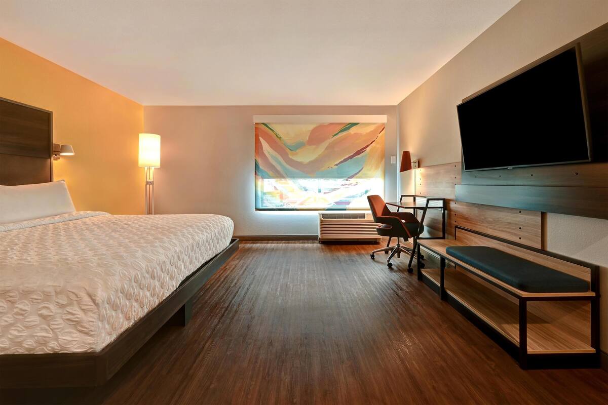 Une chambre d’hôtel équipée d’un lit, d’un bureau, d’une chaise, d’une télévision et d’une grande fenêtre donnant sur un beau paysage.