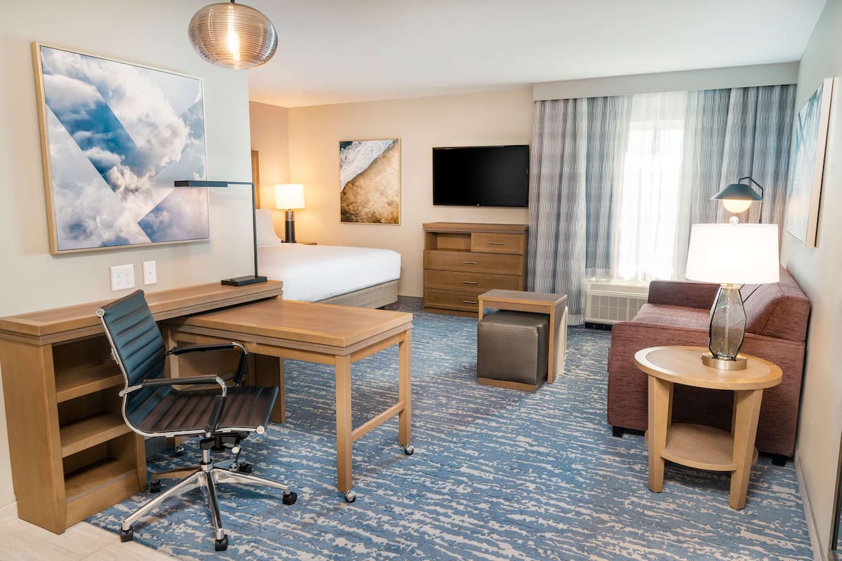 A hotel room with a bed, desk, chair, TV, and a sofa.
