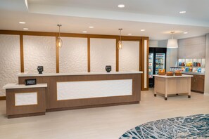 A hotel reception area with a wooden reception desk, two pendant lights, a minibar, and a refrigerator stocked with beverages. - Homewood Suites by Hilton Livermore, CA (Livermore)