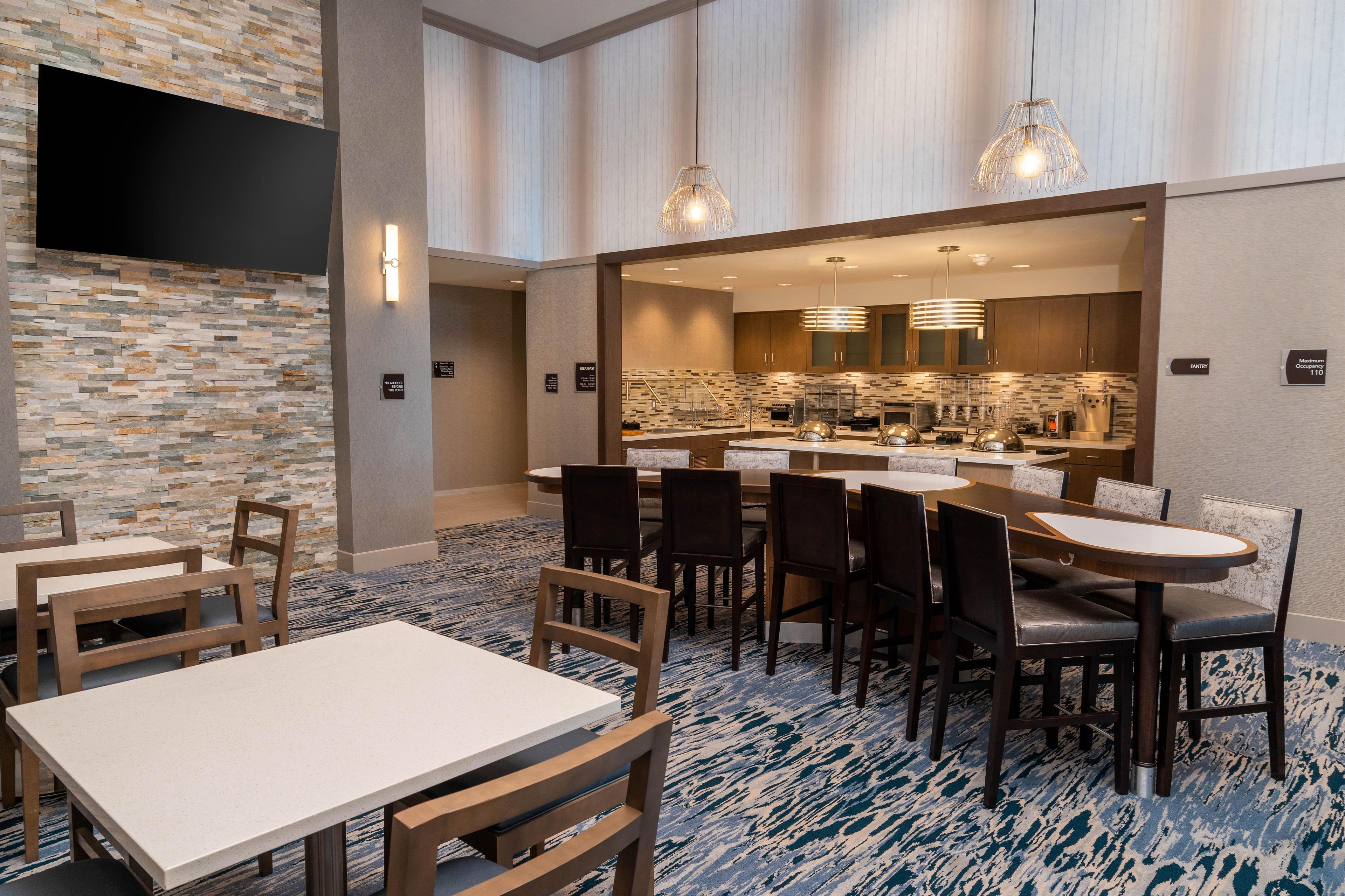 Een restaurantruimte in een hotel, met een stenen muur, een flatscreen televisie en een ontbijtbalk.