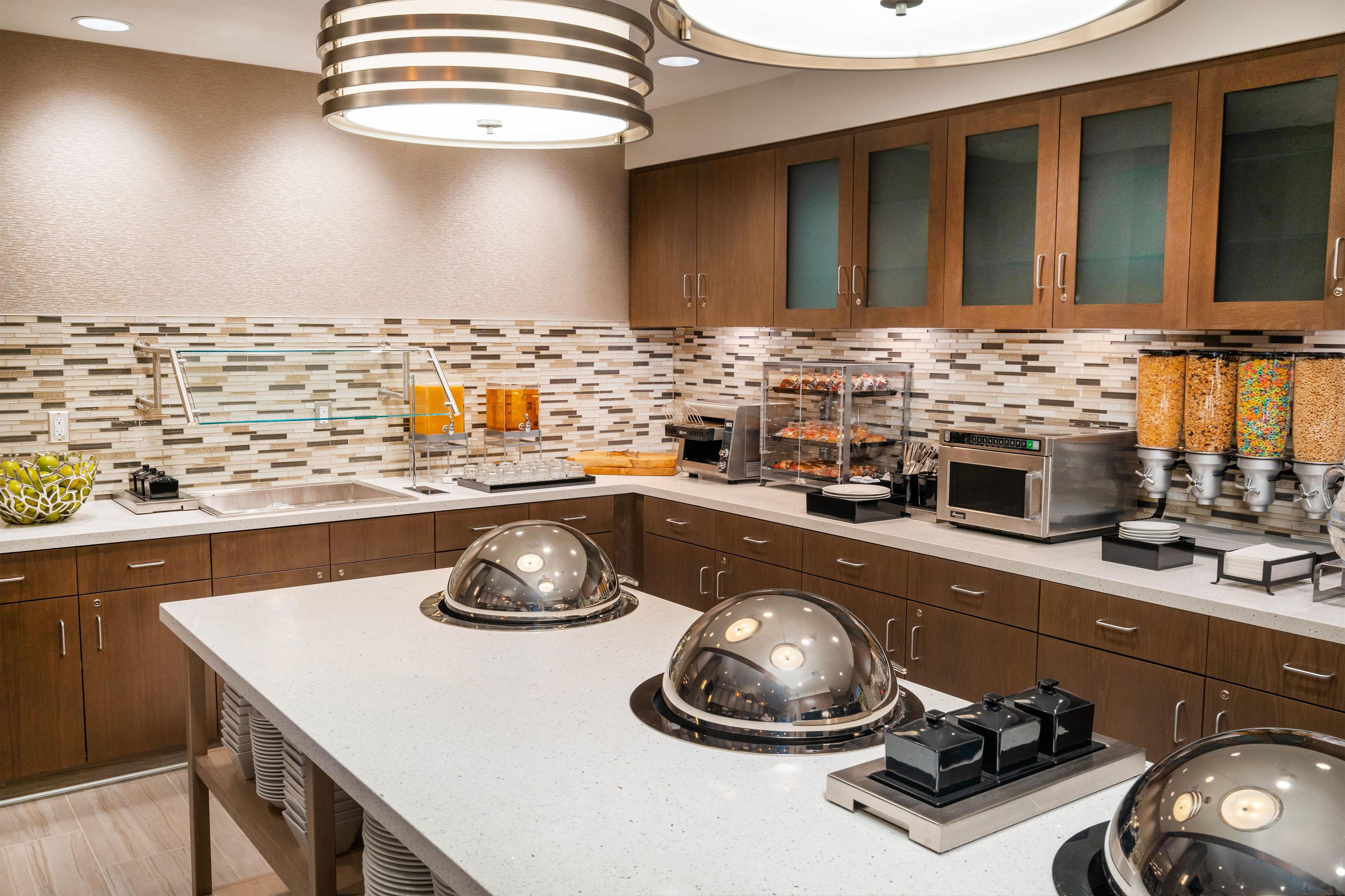 A modern kitchen with a central island, built-in appliances, and a variety of food dispensers.