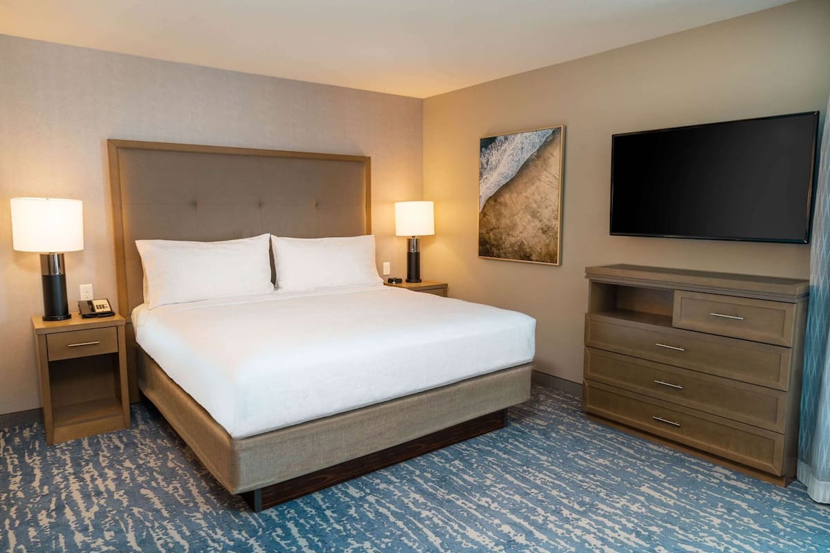 A hotel room with a large bed, two bedside tables with lamps, a flat-screen TV, and a dresser.
