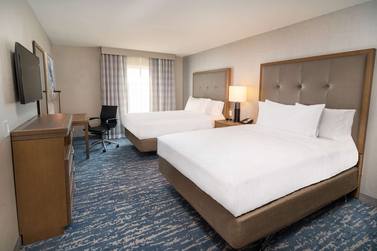 A hotel room with two beds, a desk, a chair, a TV, and a window with curtains.